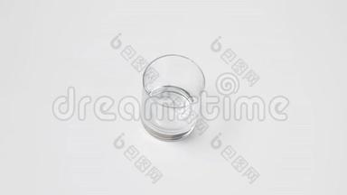 女人`手把一个透明的空玻璃放在白色的桌子上，从一个红色的罐子里倒出纯净的水，然后把拿下来